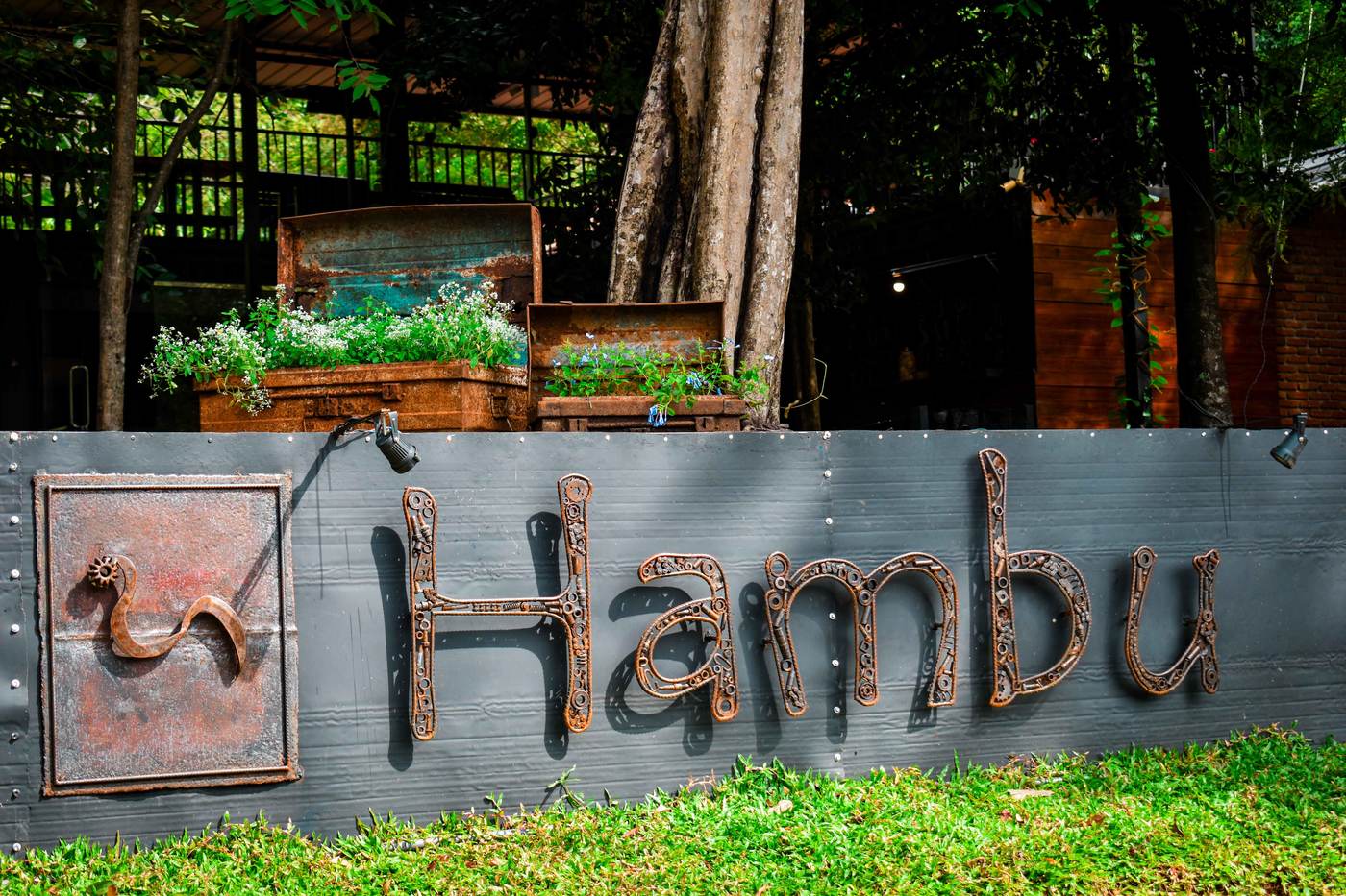 Rusted scrap-metal Hambu sign mounted on a garden wall at the café entrance