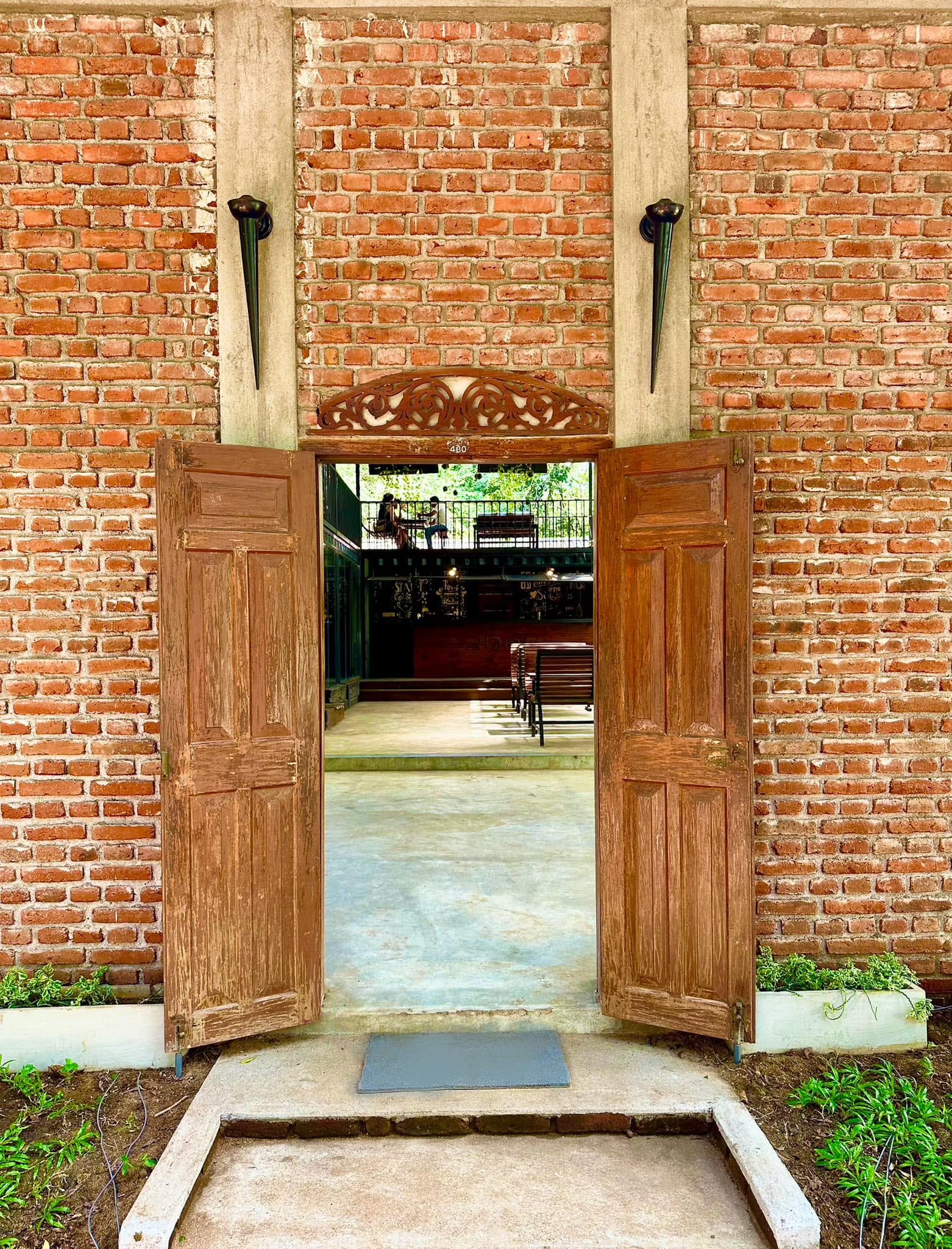 Open wooden double doors set into a brick wall at Hambu Café's entrance