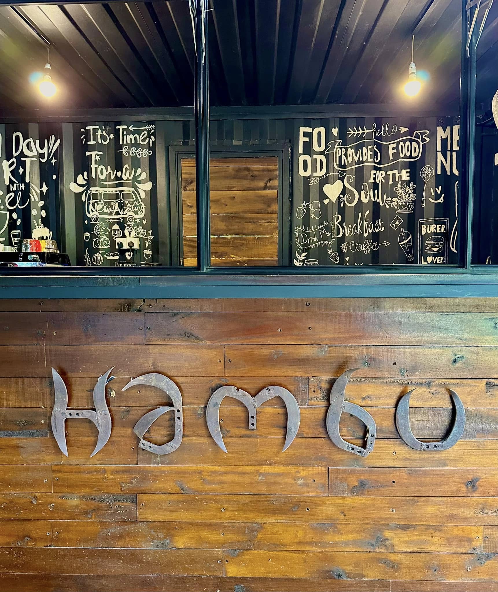 Wood-carved Hambu sign on the counter wall, with hand-painted chalkboard art behind